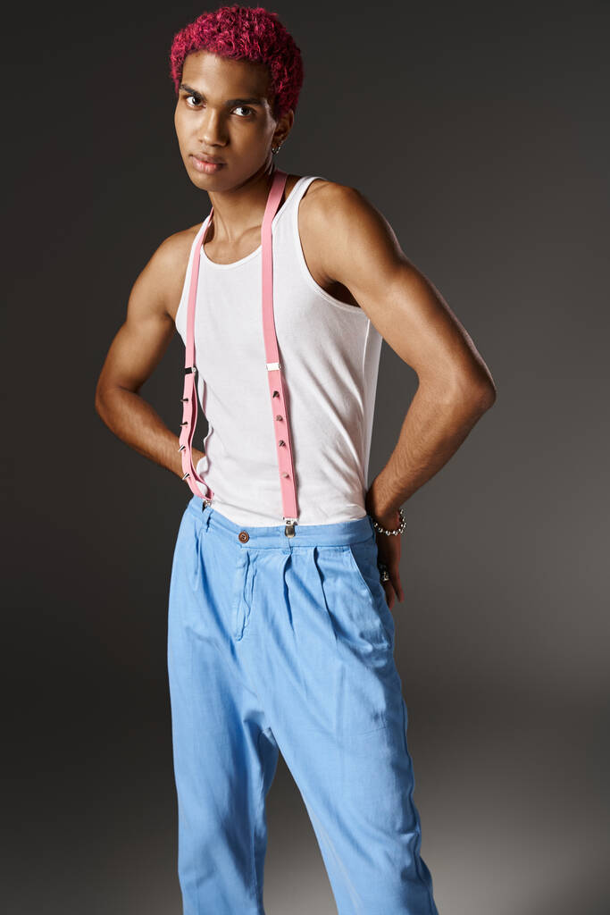 modelo masculino atractivo posando con las manos detrás en pantalones azules sobre fondo gris, moda - Foto, imagen
