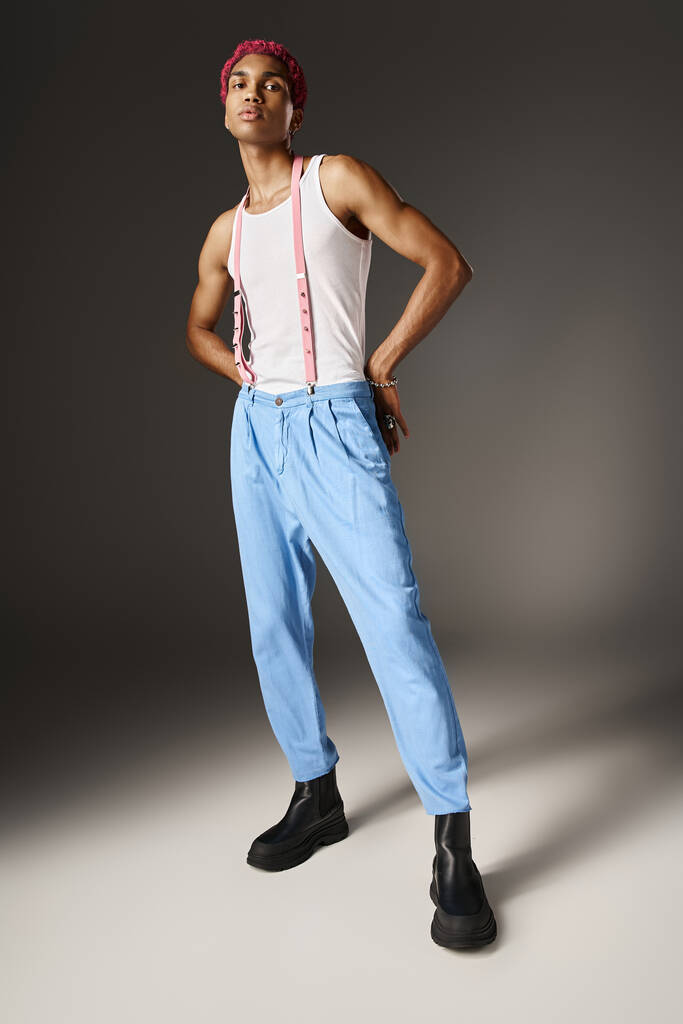 jonge voguish man in blauwe broek met bretels poseren met handen achter zijn rug, mode concept - Foto, afbeelding