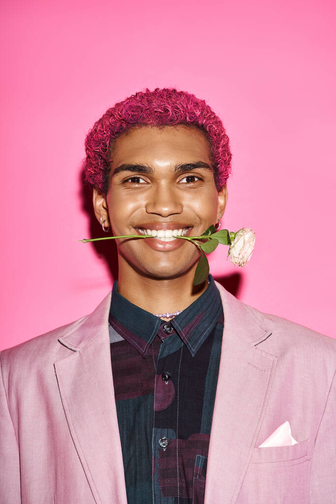 πορτρέτο του χαρούμενος νεαρός άνδρας με λευκό τριαντάφυλλο στο στόμα χαμογελώντας στην κάμερα και ενεργώντας σαν κούκλα - Φωτογραφία, εικόνα