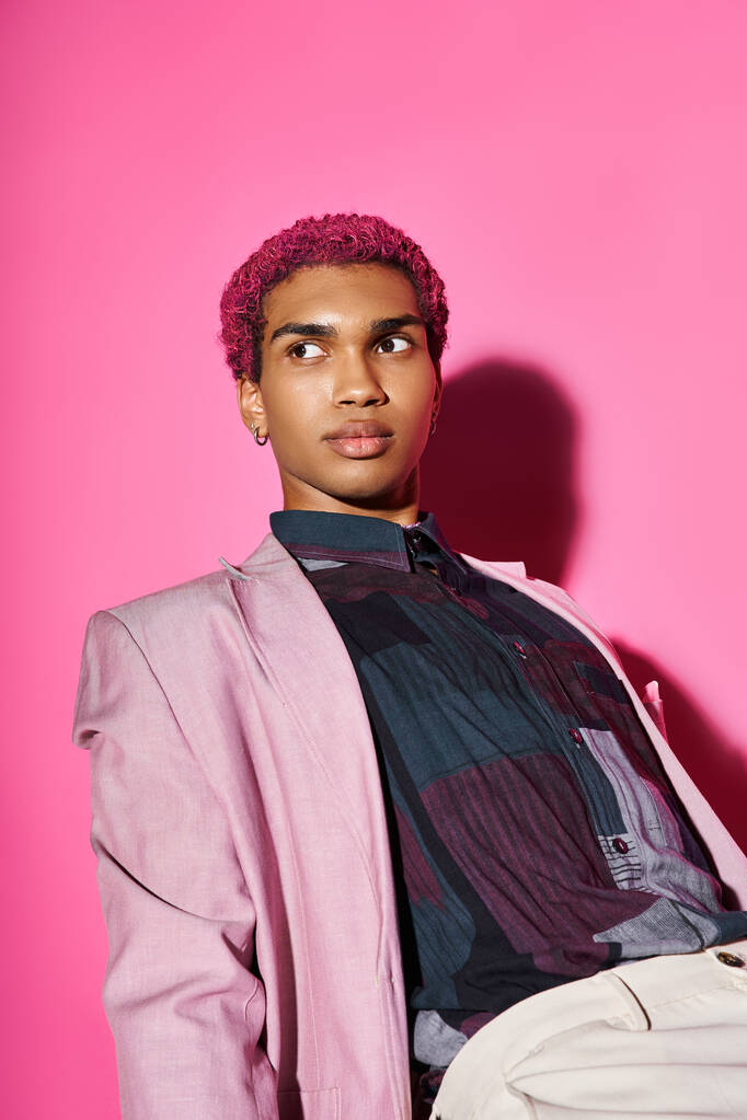 красивый мужчина с вьющимися розовыми волосами позирует на розовом фоне и смотрит в сторону на розовый фон - Фото, изображение