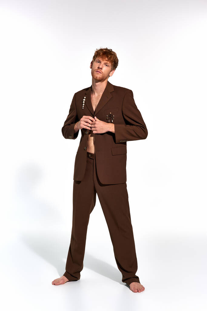 vertical shot of appealing man with red hair and beard buttoning his elegant suit on white backdrop - Photo, Image