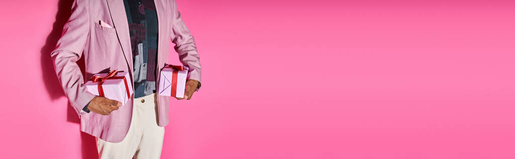 kivágott kilátás elegáns fiatalember élénk ruhában ajándékokkal a kezében rózsaszín háttér, banner - Fotó, kép