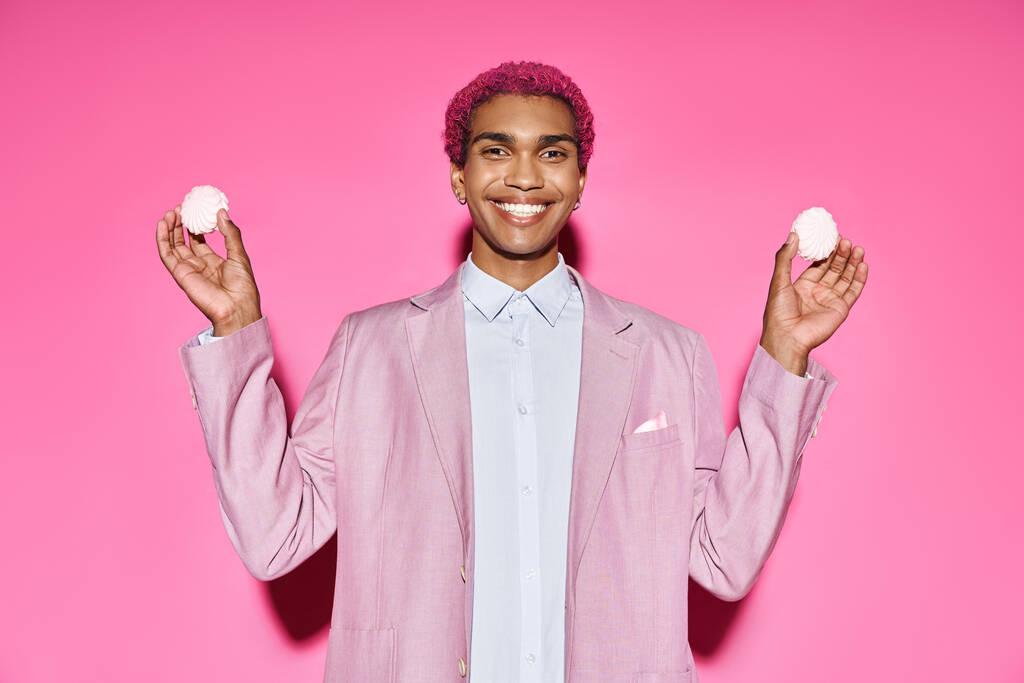 guapo joven modelo masculino sonriendo antinaturalmente y sosteniendo delicioso zefir en las manos en rosa telón de fondo - Foto, Imagen