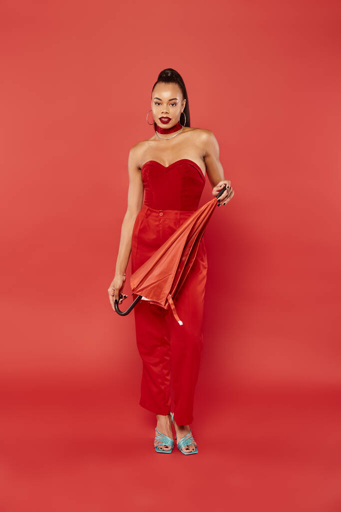 Полная длина брюнетки африканской американской модели в красной рубашке без бретелек и брюки позируют с зонтиком - Фото, изображение