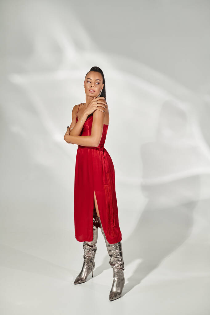 piena lunghezza di donna afro-americana in abito rosso e stivali d'argento in piedi su sfondo grigio - Foto, immagini