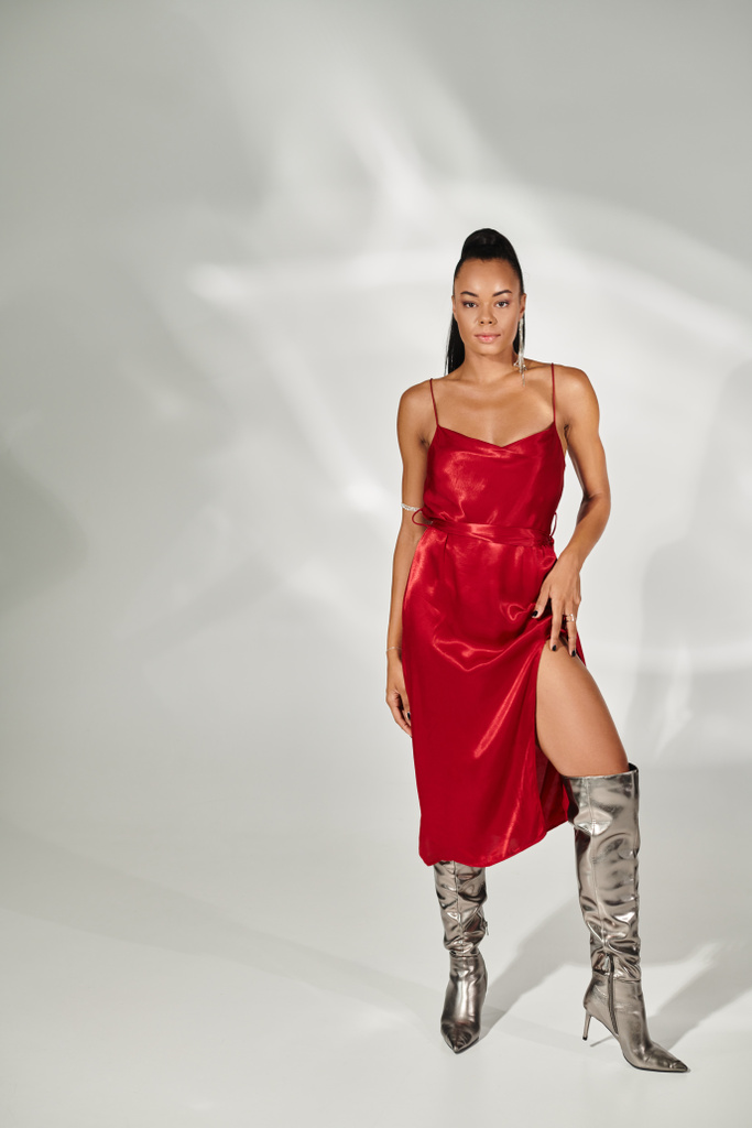 full length of seductive african american woman in red dress and silver boots on grey backdrop - Photo, Image
