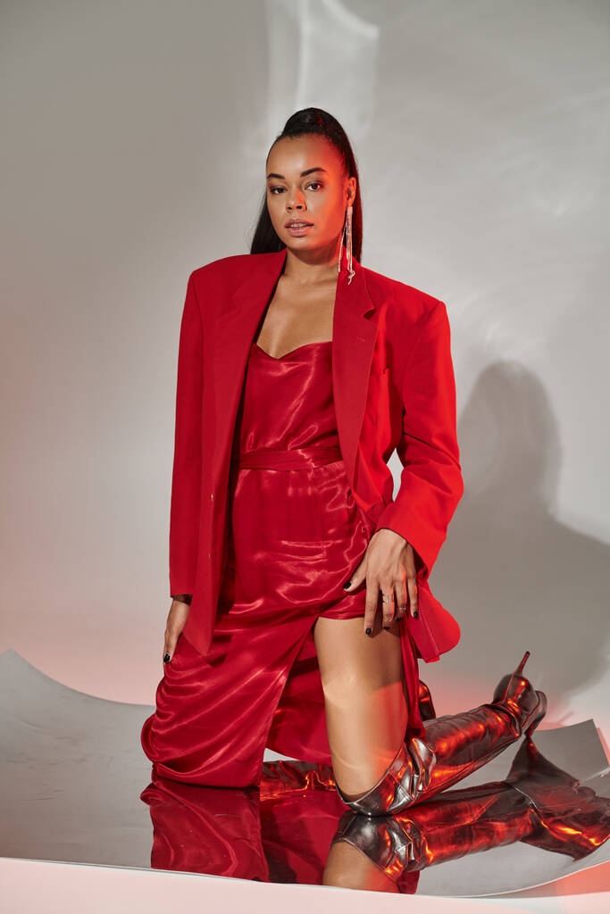 young african american woman in red dress, blazer and silver boots posing on mirrored surface - Photo, Image