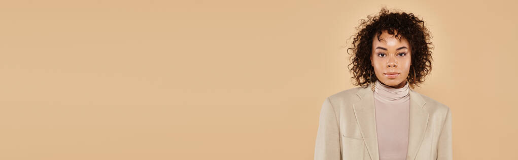 bella donna afroamericana con i capelli ricci in posa in giacca autunnale su sfondo beige - Foto, immagini
