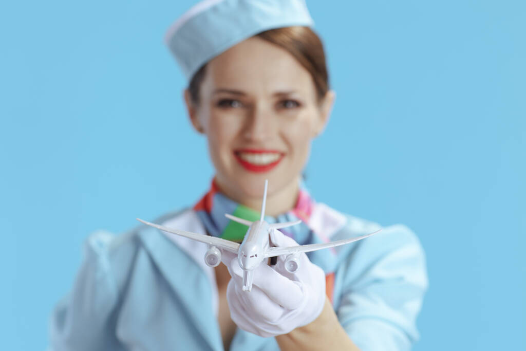 Gros plan sur une hôtesse de l'air élégante et souriante sur fond bleu en uniforme bleu avec un petit avion. - Photo, image