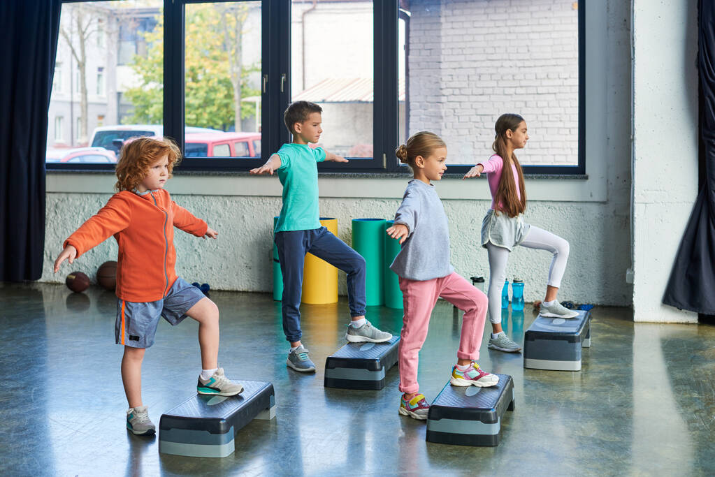 cuatro niños bonitos en ropa deportiva ejercicio con pasos de fitness con los brazos a un lado, deporte infantil - Foto, imagen