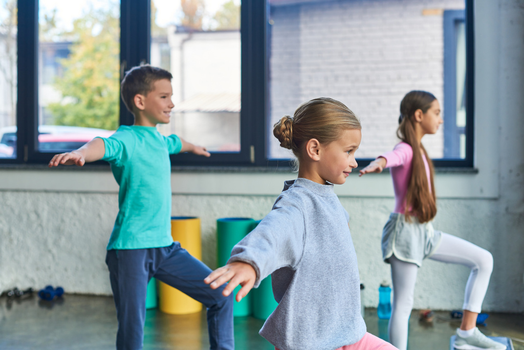 cheerful three kids in sportswear doing exercises stretching with hands asides, child sport - Photo, Image