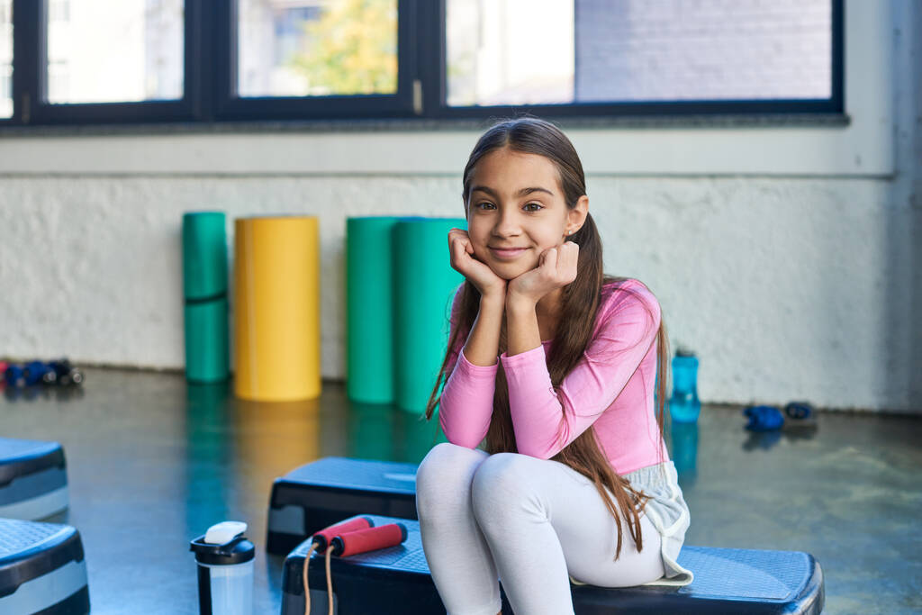 joyful dívka sedí na fitness stepper s švihadlem s úsměvem na kameru, ruce pod bradou, sport - Fotografie, Obrázek
