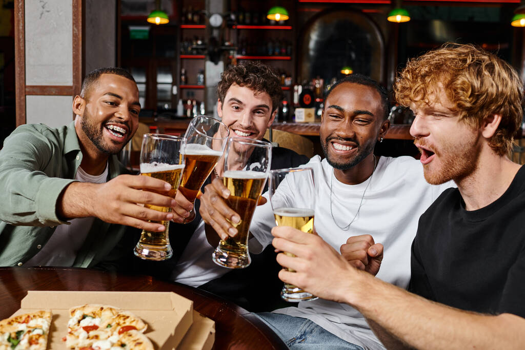 grupo de amigos masculinos interracial feliz tostando vasos de cerveza en el bar, hombres durante la despedida de soltero - Foto, Imagen