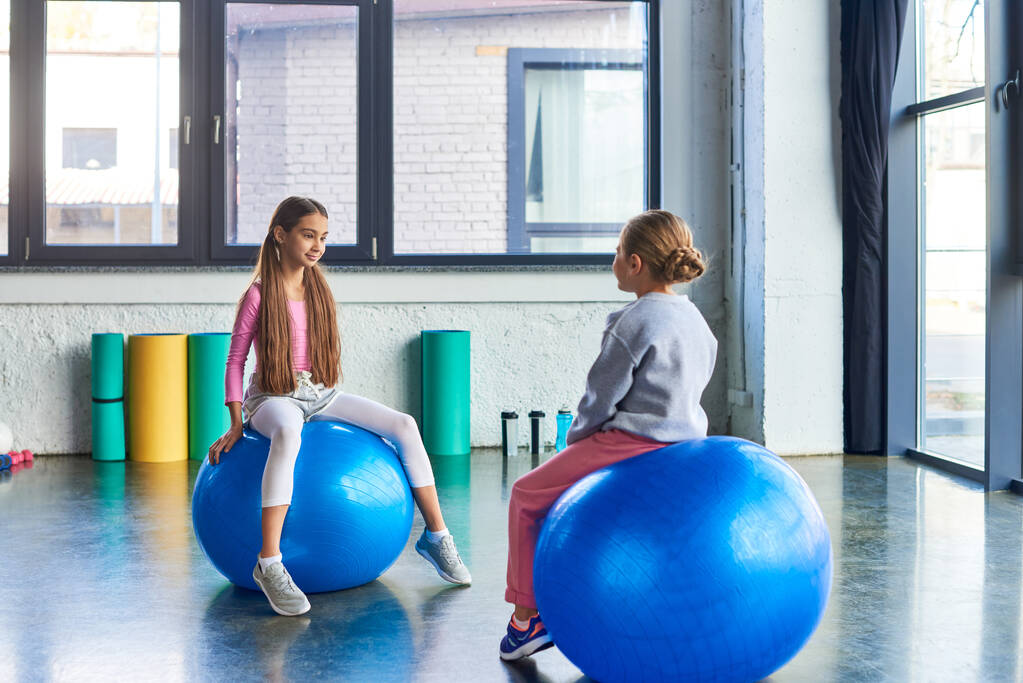 pretty little girls in sportswear sitting on fitness balls and looking at each other, child sport - Photo, Image