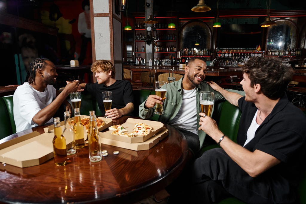 щасливі міжрасові друзі чоловічої статі спілкуються піцою і келихами пива в барі, чоловіки на дівич-вечірці - Фото, зображення