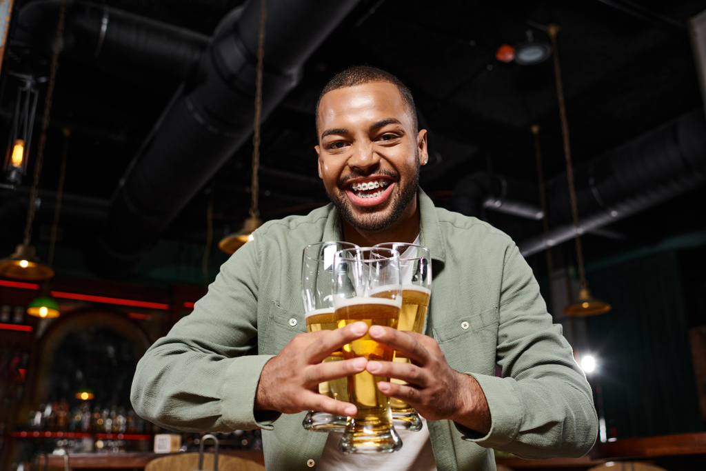 gelukkig Afrikaans amerikaanse man met beugels met drie glazen bier in de bar, plezier hebben in het weekend - Foto, afbeelding