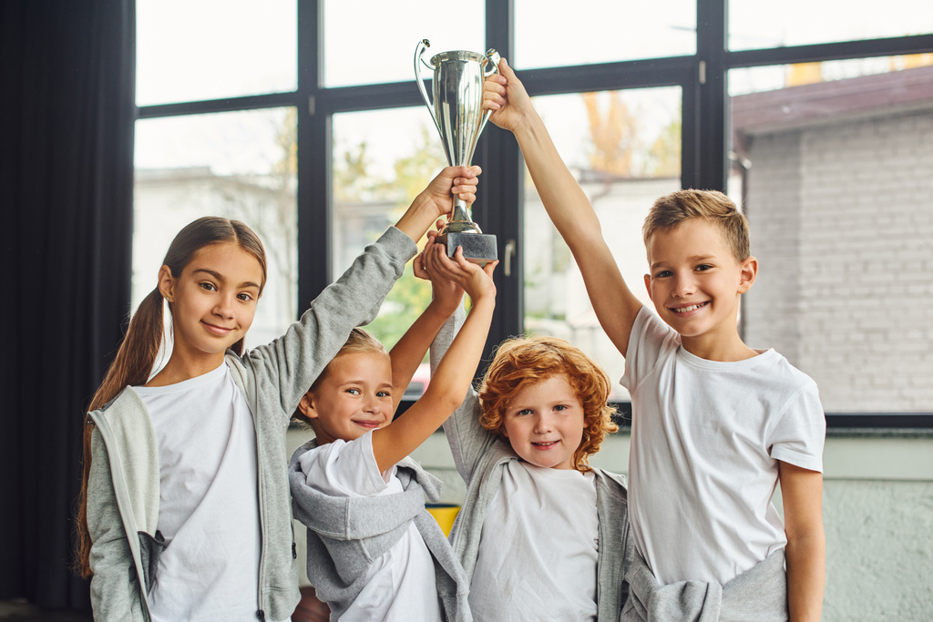 torcendo meninos e meninas pré-adolescentes em sportswear levantando troféu acima das cabeças, esporte infantil - Foto, Imagem