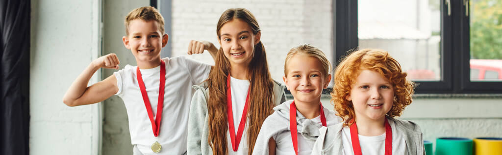 Glückliche Kinder in Sportbekleidung mit goldenen Medaillen, die freudig in die Kamera lächeln, Kindersport, Banner - Foto, Bild