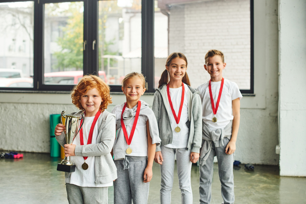 Neşeli küçük kızlar ve oğlanlar gülümseyip poz veriyorlar altın madalyayla, çocuk sporu - Fotoğraf, Görsel