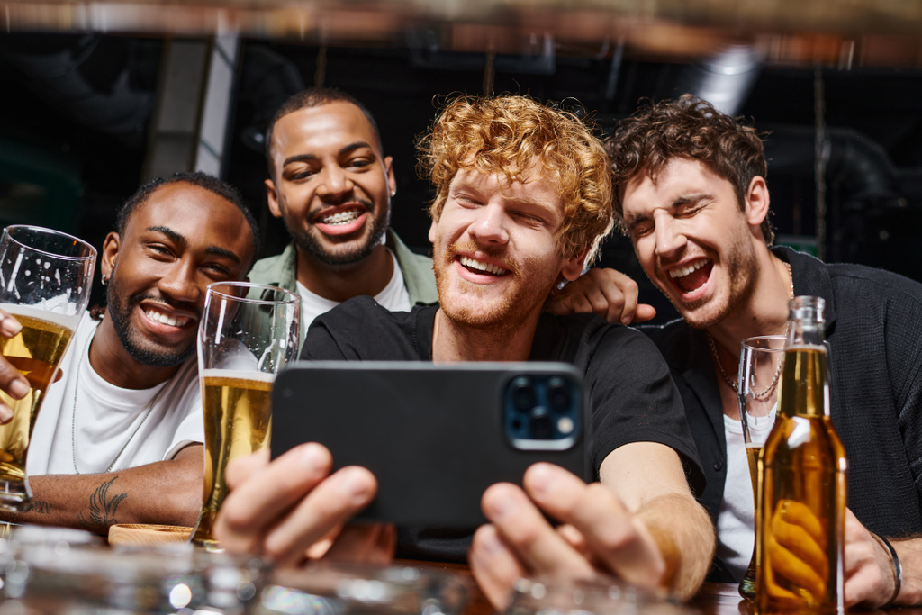 pozitív fajok közötti férfiak szelfit készítenek okostelefonon, és sörrel a kezükben legénybúcsún a bárban - Fotó, kép