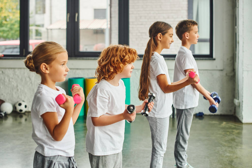 négy kis csinos gyerek sportruhában pózol profilban, miközben súlyzókkal edz, sport - Fotó, kép