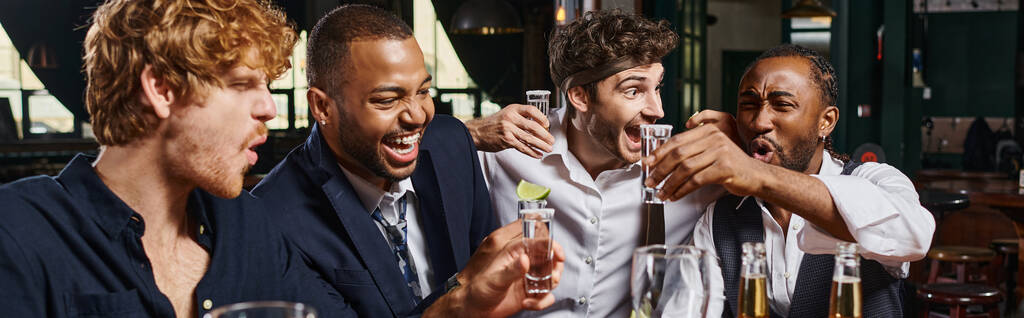 izgatott többnemzetiségű barátok kezében tequila felvételek lime mellett pohár sör a bárban, banner - Fotó, kép