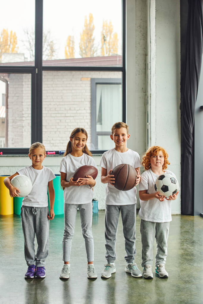 ripresa verticale di quattro bambini preadolescenti con diversi tipi di palle, sorridenti alla macchina fotografica, sport - Foto, immagini