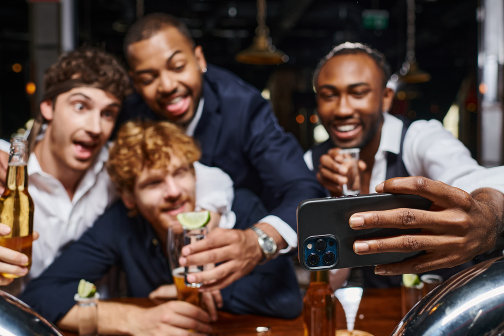 alegres colegas multiétnicos en ropa formal tomando selfie en el teléfono inteligente en el bar después del trabajo - Foto, Imagen