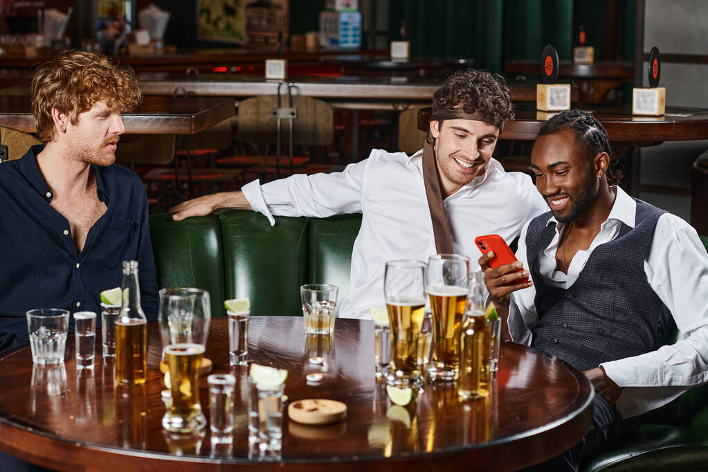 šťastný africký Američan pomocí smartphone a trávit čas s kolegy po práci v baru - Fotografie, Obrázek