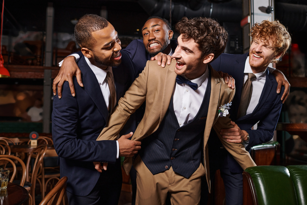 холостяцька вечірка, щасливі міжрасові чоловіки вітають друга в барі, кращих чоловіків і нареченого в костюмах - Фото, зображення