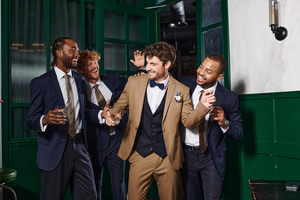 холостяцька вечірка, багатоетнічні найкращі чоловіки і сміх нареченого, стоячи в келихах віскі - Фото, зображення