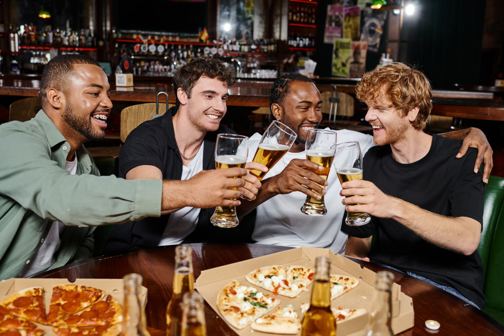 noche, alegres hombres multiétnicos tintineo vasos de cerveza cerca de pizza en el bar, amistad masculina - Foto, imagen