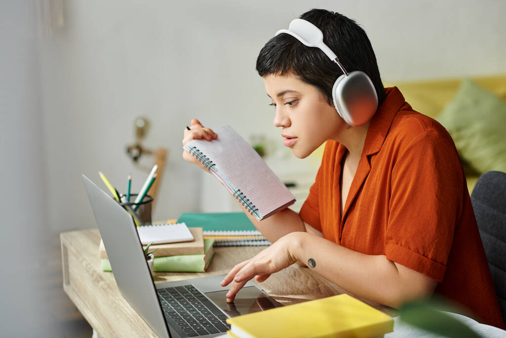 jovem estudante do sexo feminino em roupa casual com tatuagem estudando no laptop segurando notas, educação - Foto, Imagem