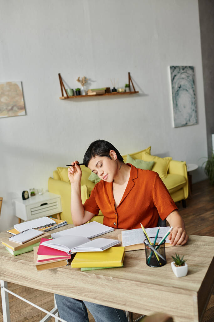 вертикальный кадр трудолюбивого уставшего студента, сидящего за столом с ручкой в руке, читающего учебник - Фото, изображение