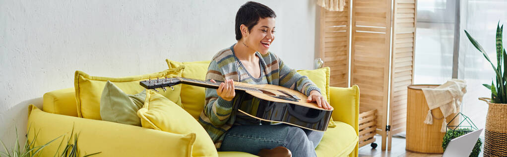 ευτυχισμένη γυναίκα με κοντά μαλλιά κρατώντας κιθάρα κατά τη διάρκεια του μαθήματος απομακρυσμένης μουσικής, εκπαίδευση στο σπίτι, πανό - Φωτογραφία, εικόνα