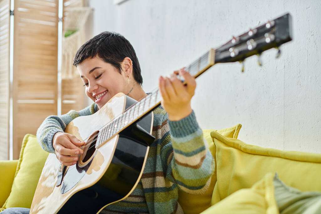 χαρούμενη ελκυστική γυναίκα με κοντά μαλλιά σε απομακρυσμένο μάθημα κιθάρας χαμογελώντας χαρούμενα, εκπαίδευση στο σπίτι - Φωτογραφία, εικόνα