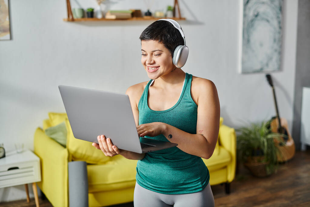 mujer joven feliz con el ordenador portátil y auriculares que asisten a la lección de fitness remota, fitness y deporte - Foto, imagen