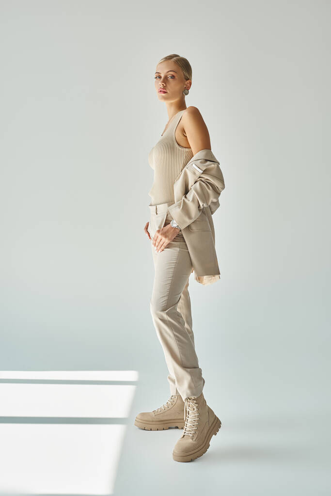 piena lunghezza della donna alla moda in total beige abbigliamento casual in piedi su sfondo grigio alla luce del sole - Foto, immagini