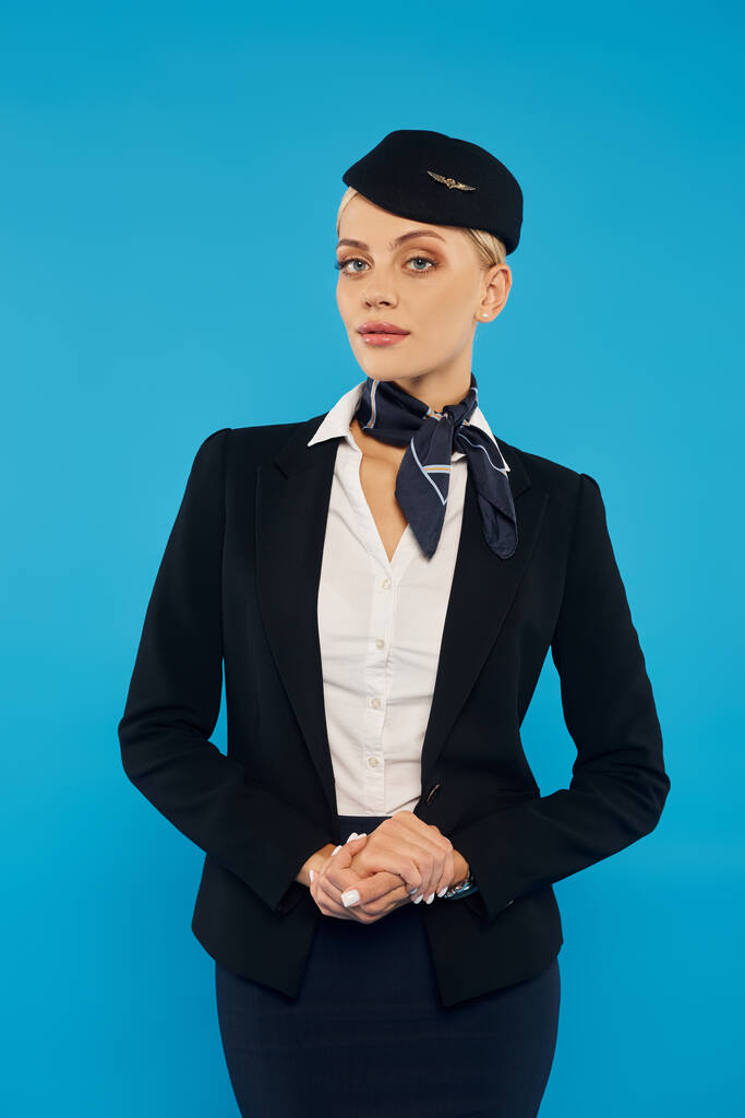 mladá atraktivní letuška v elegantní uniformě dívající se na kameru na šedém pozadí, snímek hlavy - Fotografie, Obrázek