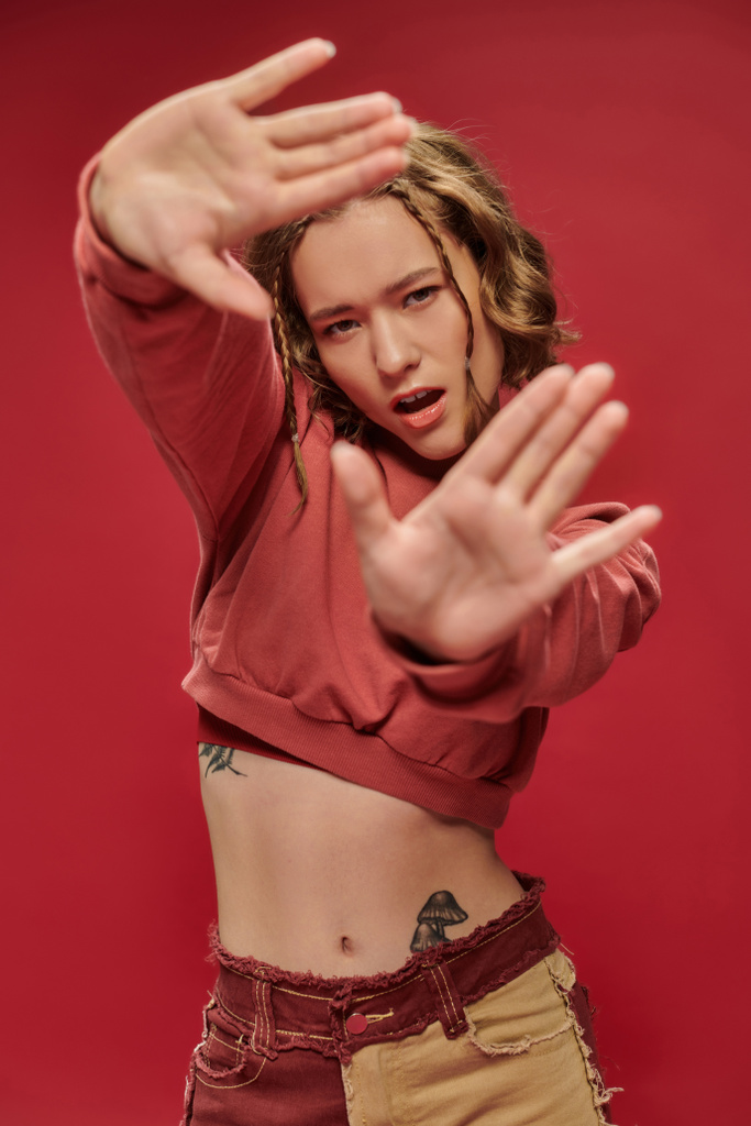 самовыражение, стильная молодая женщина в обрезанном длинном рукаве с жестом в рамке с руками на красном - Фото, изображение