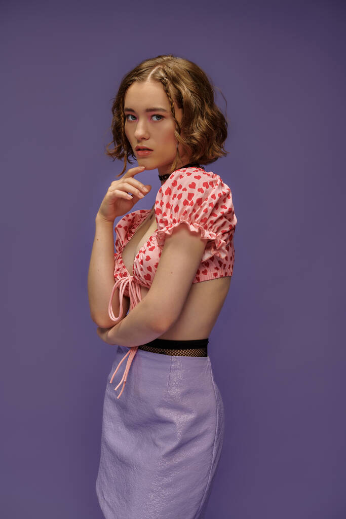 nachdenkliche junge Frau in abgeschnittenem Top und Rock, die das Kinn auf lila Hintergrund berührt, persönlicher Stil - Foto, Bild