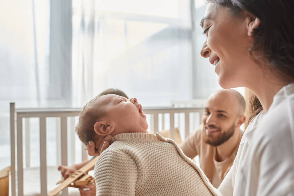focus on happy mother looking at her newborn baby with blurred joyful father on backdrop, family - Photo, Image