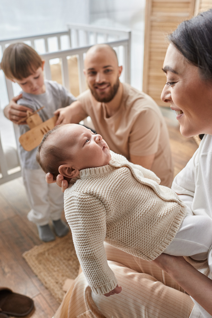 vertical focused shot of jolly mother holding baby boy in front of blurred husband and little son - Photo, Image