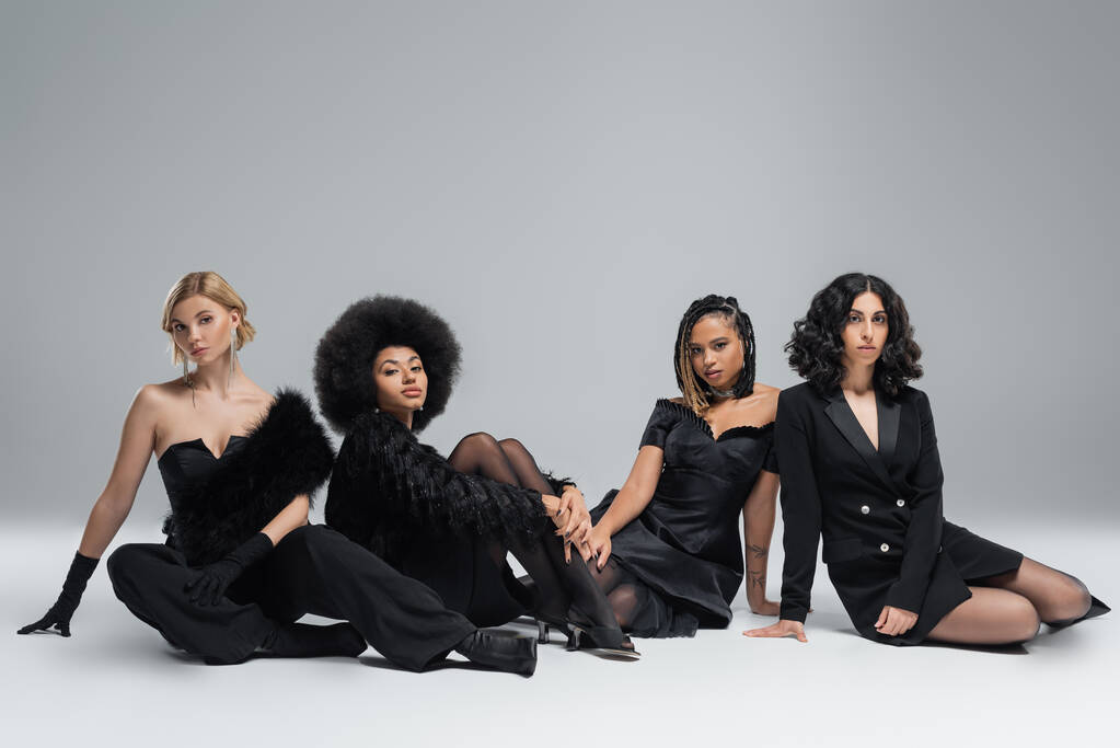 Gruppe auf eleganten multirassischen Freundinnen in schwarzen Outfits sitzt auf grau, Vielfalt in High Fashion - Foto, Bild