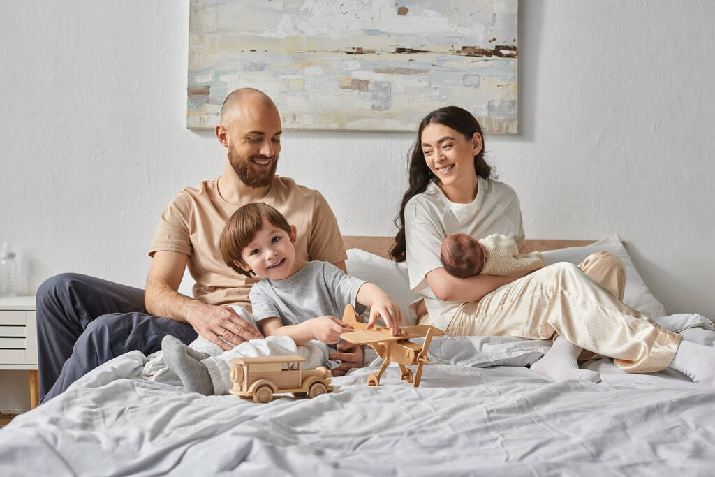 vreugdevolle familie met een geweldige tijd samen ontspannen in bed en glimlachen naar elkaar, moderne ouderschap - Foto, afbeelding