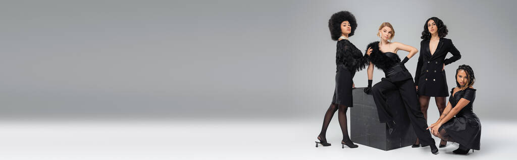 monikulttuurinen tyttöystäviä tumma tyylikäs puku poseeraa lähellä musta kuutio harmaa, vaakasuora banneri - Valokuva, kuva