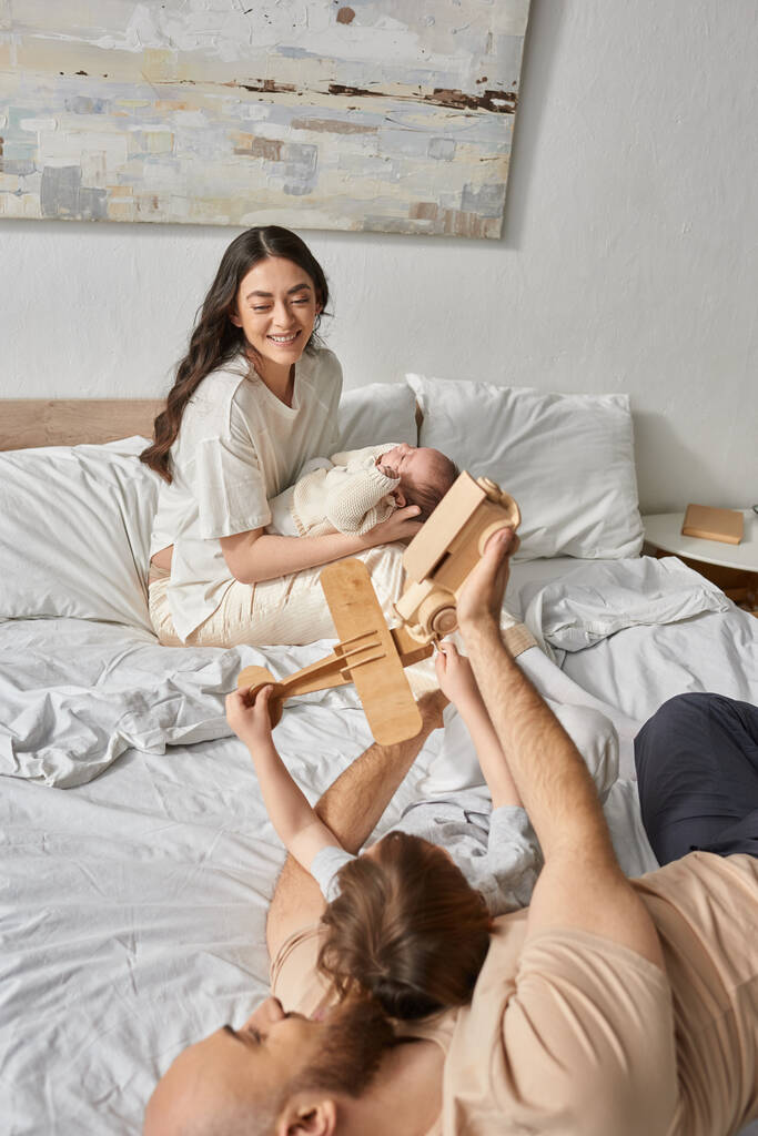 весела мати тримає новонароджену дитину, яка щасливо дивиться на свого чоловіка, граючи зі своїм маленьким сином - Фото, зображення