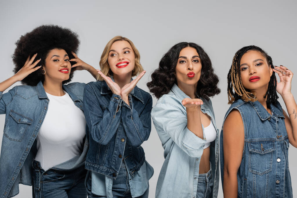 multiracial woman blowing air kiss near happy charming girlfriends posing in denim clothes on grey - Photo, Image