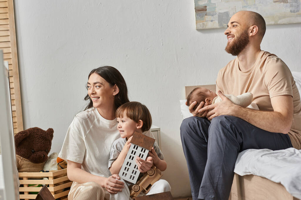 радісна щаслива сім'я в комфортному домашньому вбранні, радісно посміхаючись і озираючись, сучасне батьківство - Фото, зображення