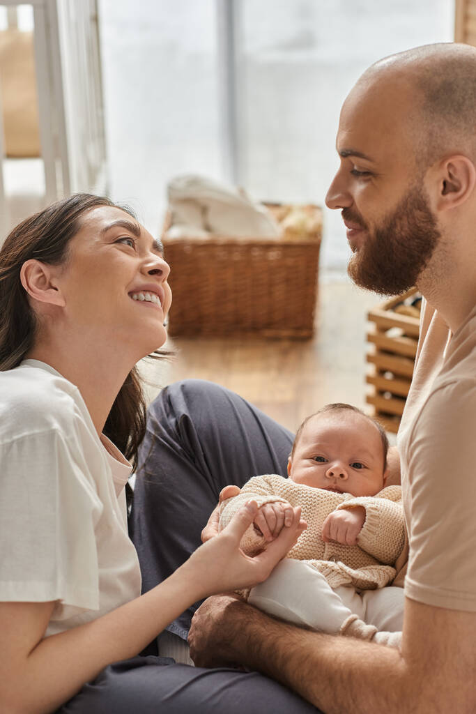 vertical shot of happy couple smiling at each other and holding their newborn baby boy, family - Photo, Image